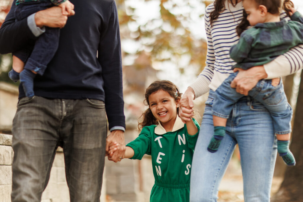 Young girl holding mom and dad's hands while they also each hold another kid.