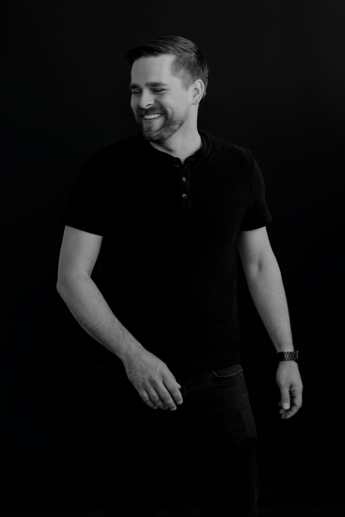 Man in black shirt looking off to the side laughing while walking.